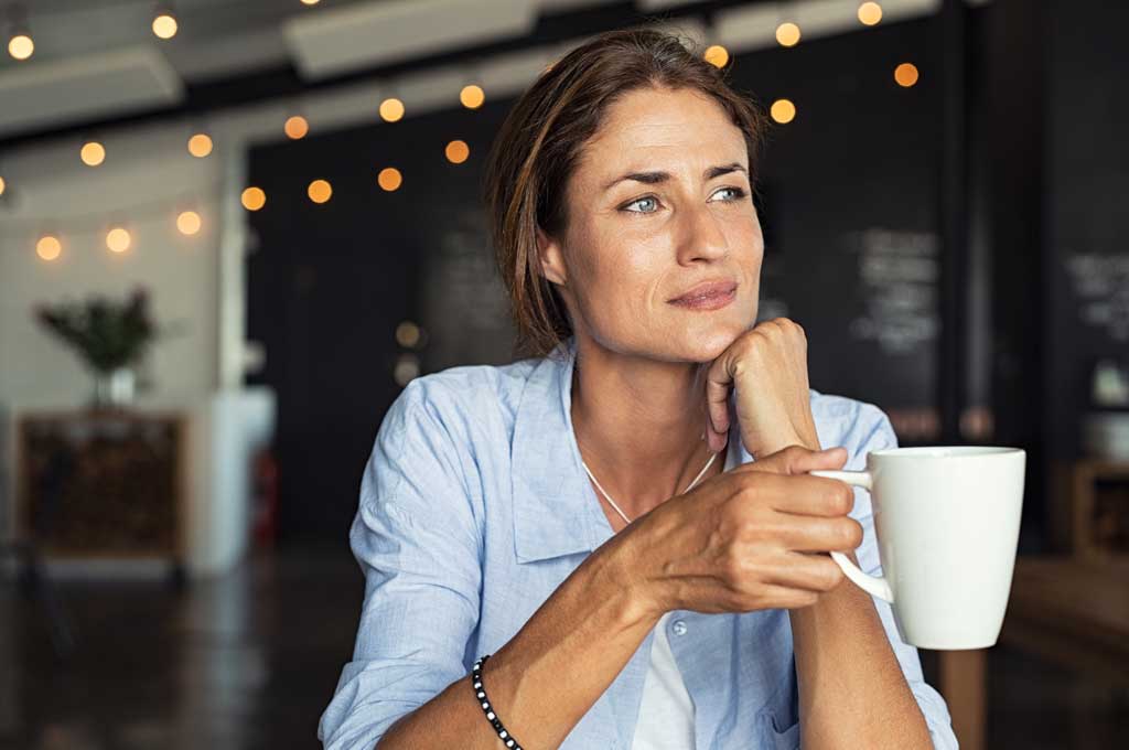 Middle aged woman holding coffee cup staring dreamily